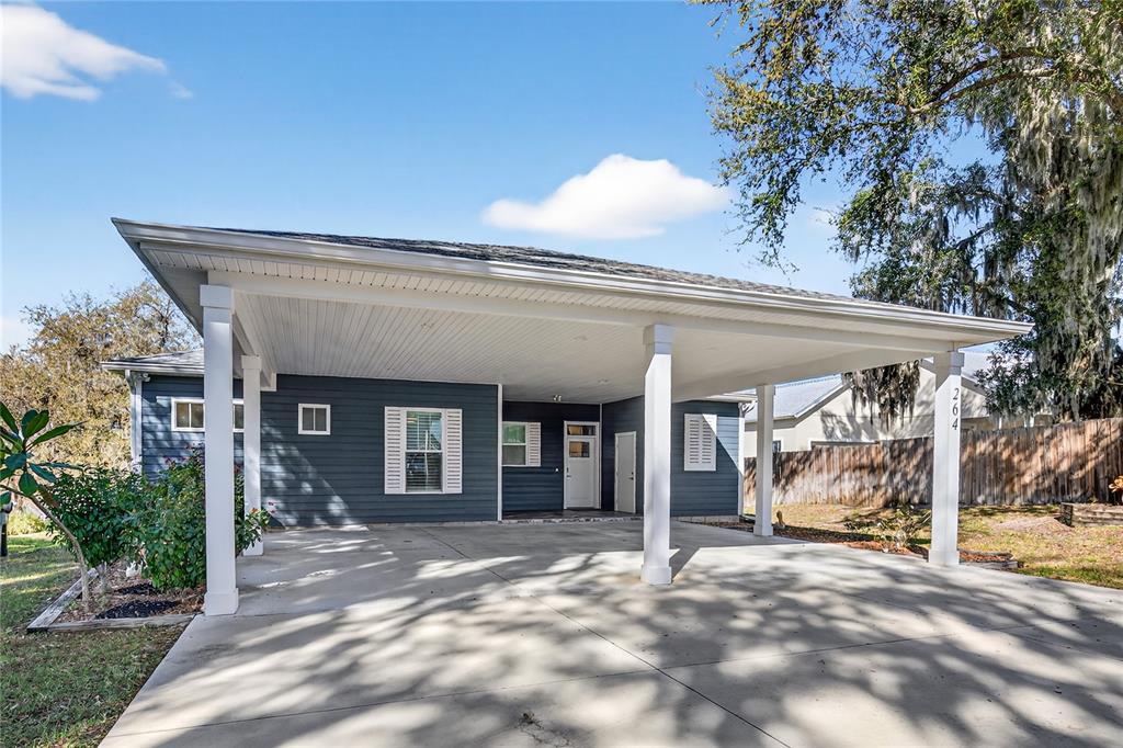 A blue-sided house features a large concrete carport with white support pillars and trim — 264 S CENTRAL AVENUE, UMATILLA, FL