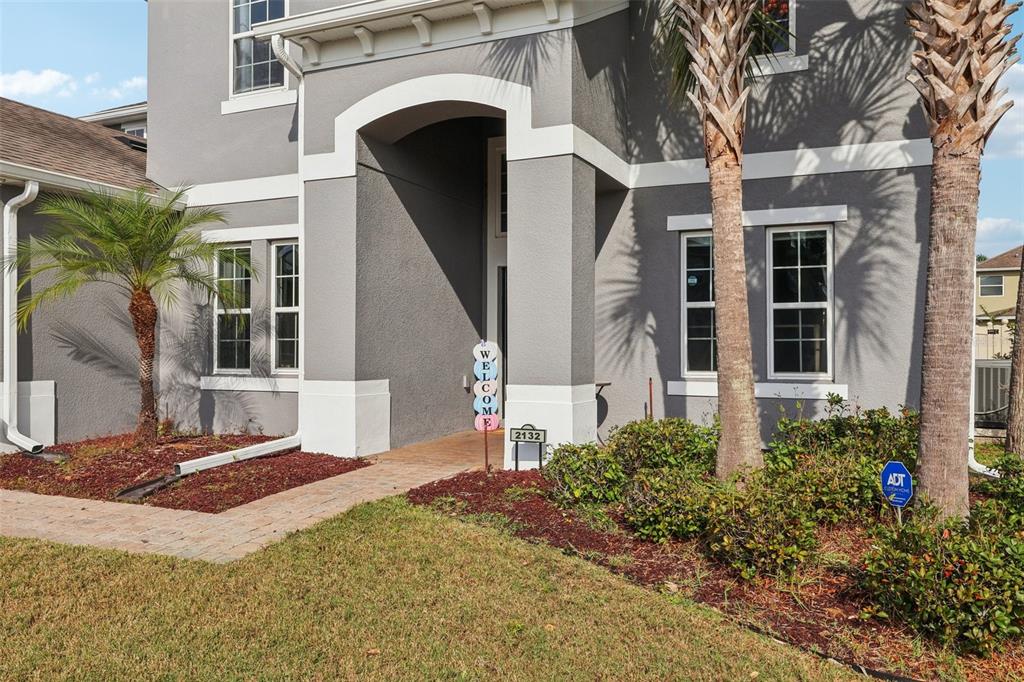 A gray two-story house features a covered entryway, palm trees, and a paved walkway — 2132 PLANTATION OAK DR, ORLANDO, FL