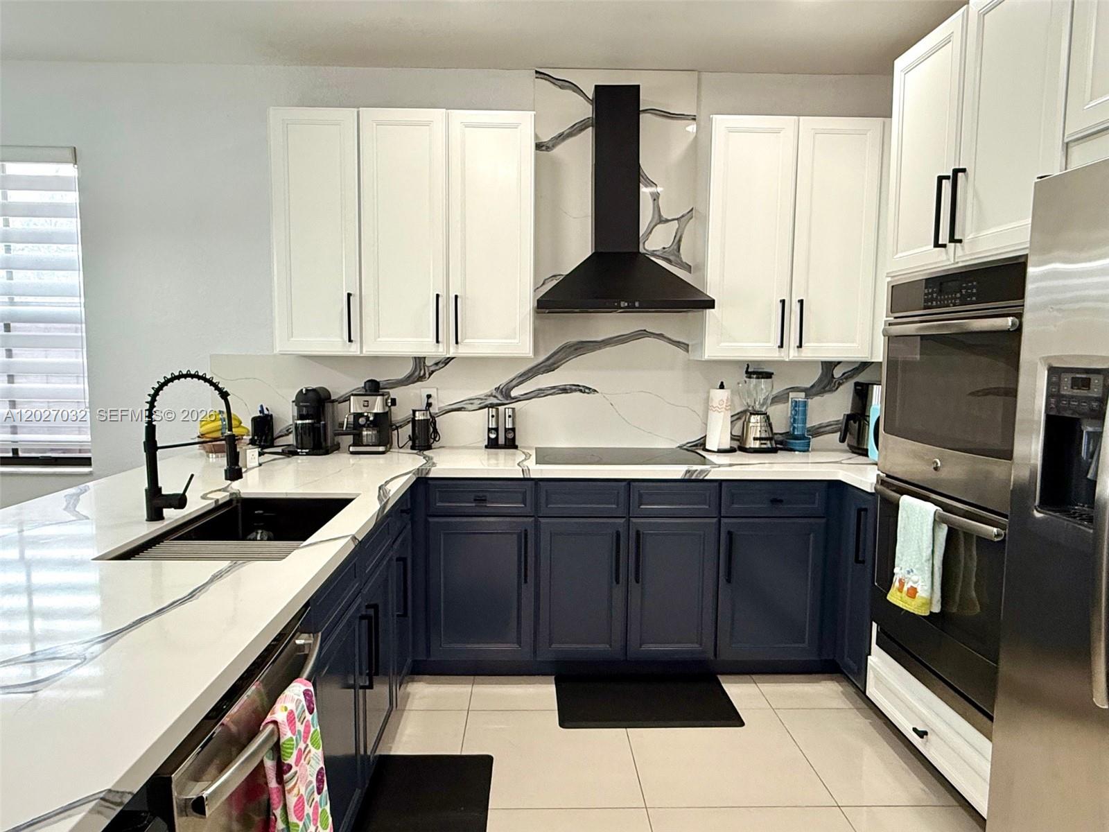 A kitchen features white upper cabinets, navy lower cabinets, and a unique branch-patterned backsplash — 10060 NW 86th Ter, Doral FL 33178, DORAL, FL