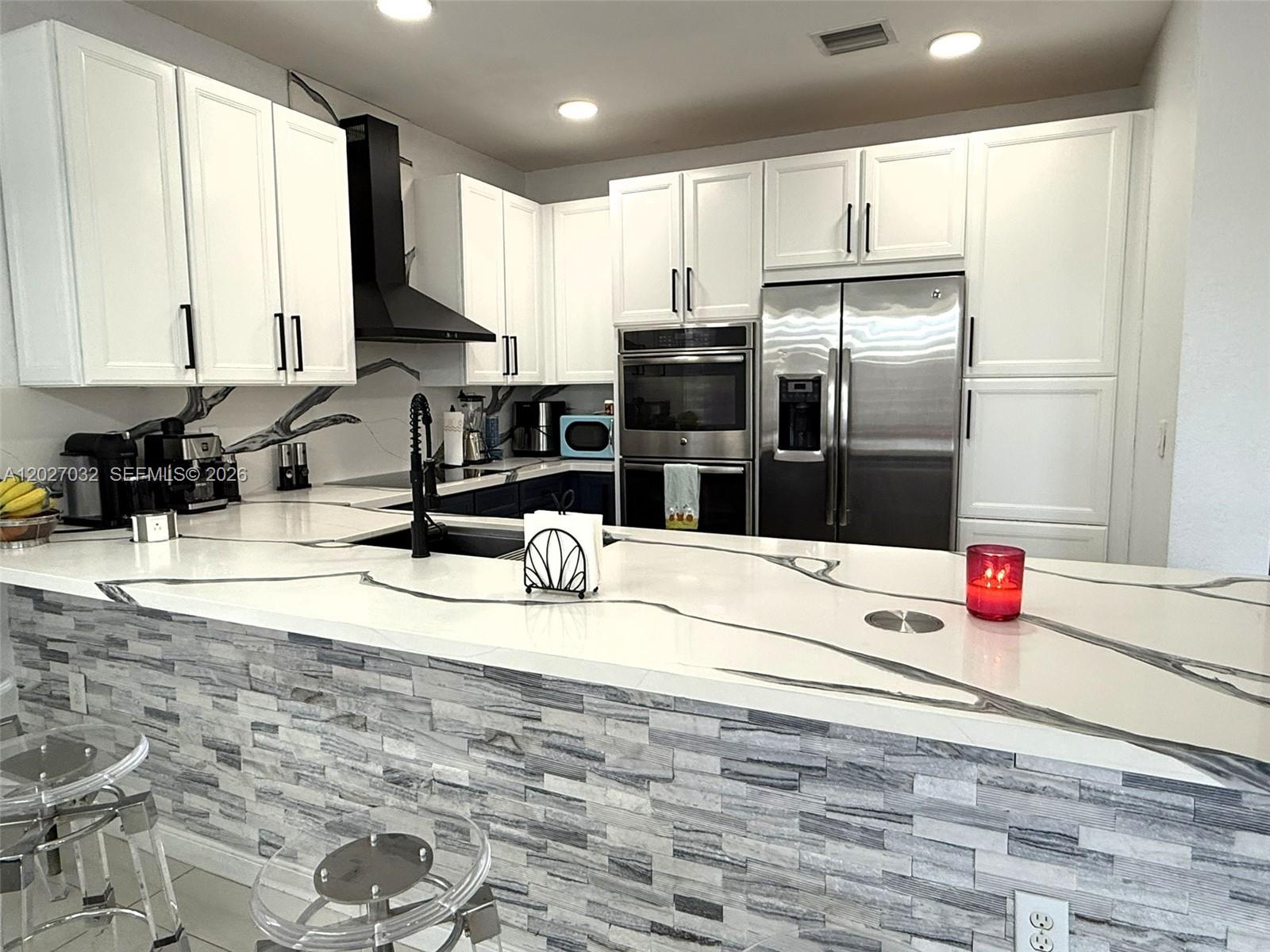 A modern kitchen features white cabinets, stainless steel appliances, and a stone-tiled breakfast bar — 10060 NW 86th Ter, Doral FL 33178, DORAL, FL