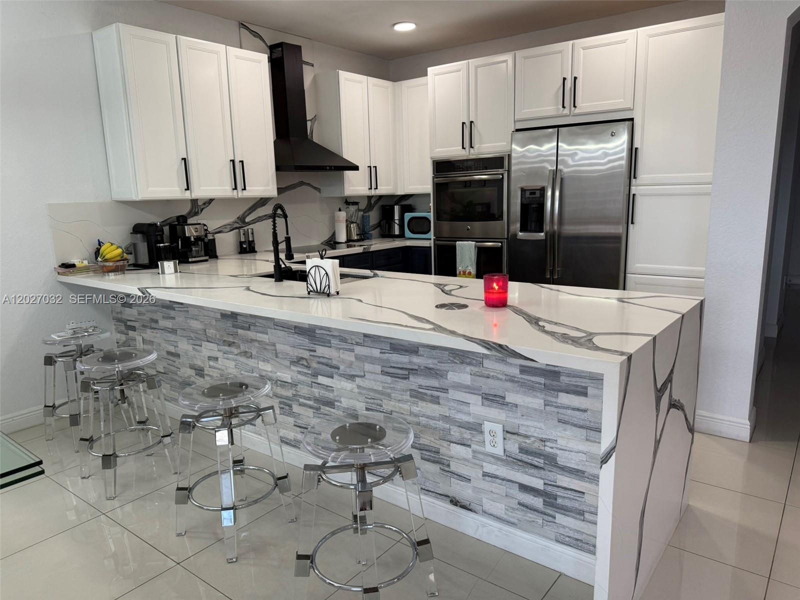 A modern kitchen features white cabinets, a waterfall quartz island, and a stone-tiled breakfast bar — 10060 NW 86th Ter, Doral FL 33178, DORAL, FL