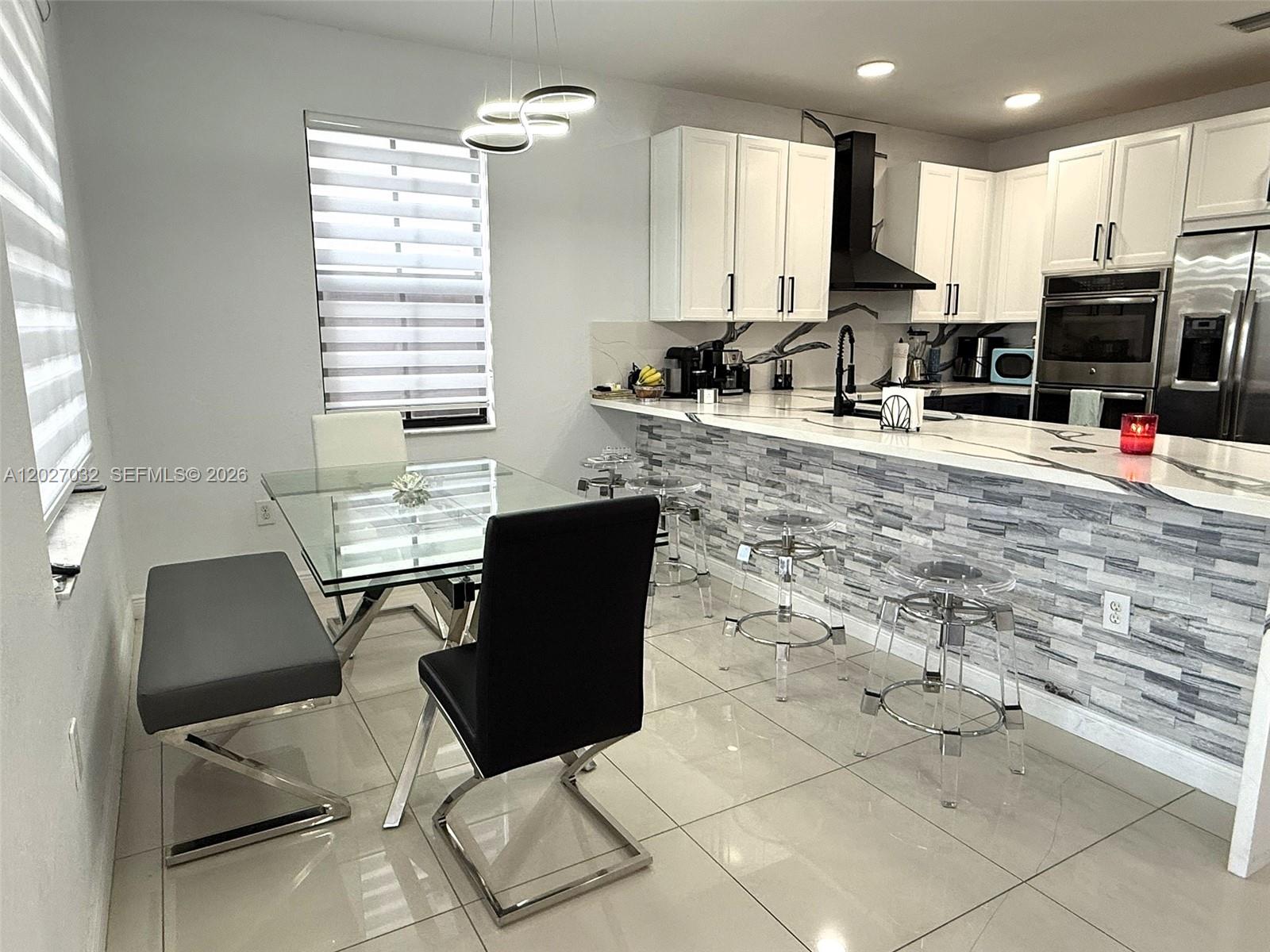 A modern kitchen features white cabinetry, a stone-tiled breakfast bar, and a glass dining table — 10060 NW 86th Ter, Doral FL 33178, DORAL, FL