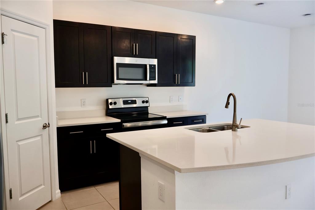 A kitchen features dark cabinets, white countertops, a central island, and stainless steel appliances — 3635 DAVENPORT CREEK COURT, KISSIMMEE, FL