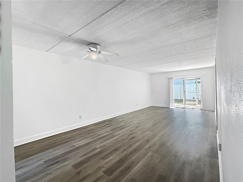 An empty living room features white walls, a textured ceiling, and gray wood-look flooring — 4435 1ST STREET NE UNIT 103, ST PETERSBURG, FL
