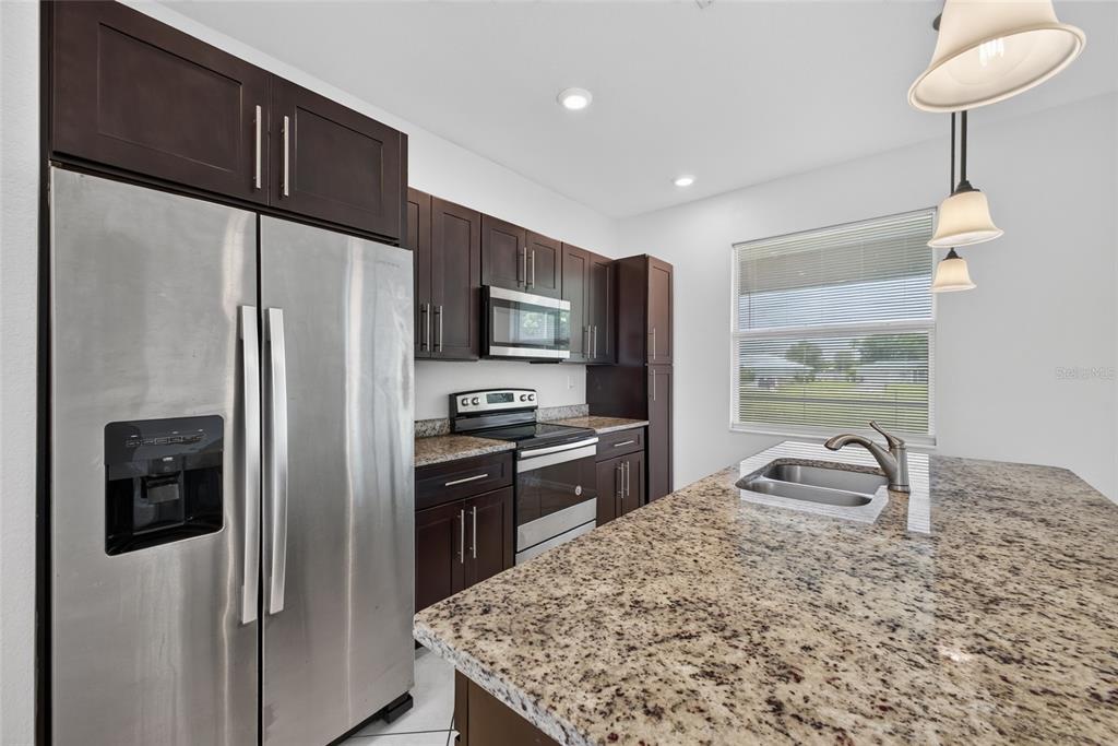 A kitchen features dark wood cabinets, granite countertops, stainless steel appliances, and a center island — 2714 NW 1ST PLACE, CAPE CORAL, FL