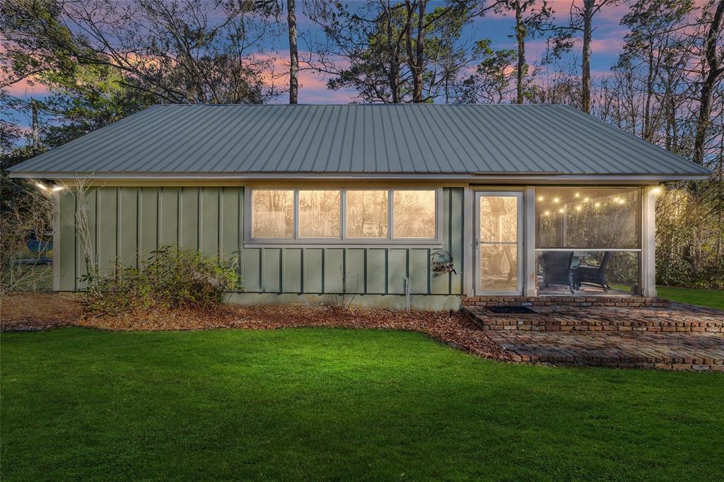 A green house with a metal roof, large windows, and a screened-in porch with brick flooring — 10801 SW 185TH TERRACE, DUNNELLON, FL