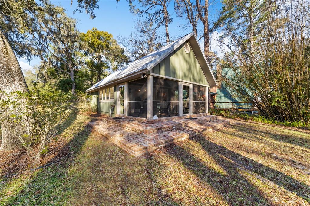 A small cabin with a metal roof and a screened porch sits on a brick patio — 10801 SW 185TH TERRACE, DUNNELLON, FL