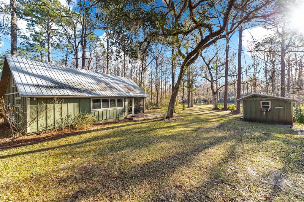 A green cabin with a metal roof stands next to a small matching shed — 10801 SW 185TH TERRACE, DUNNELLON, FL