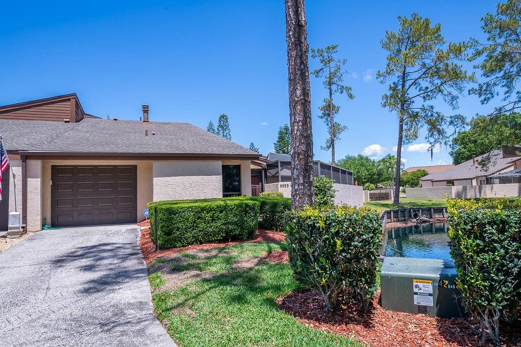 A single-story house with a garage, driveway, and landscaping sits beside a small pond — 5003 UMBER WAY S, TAMPA, FL