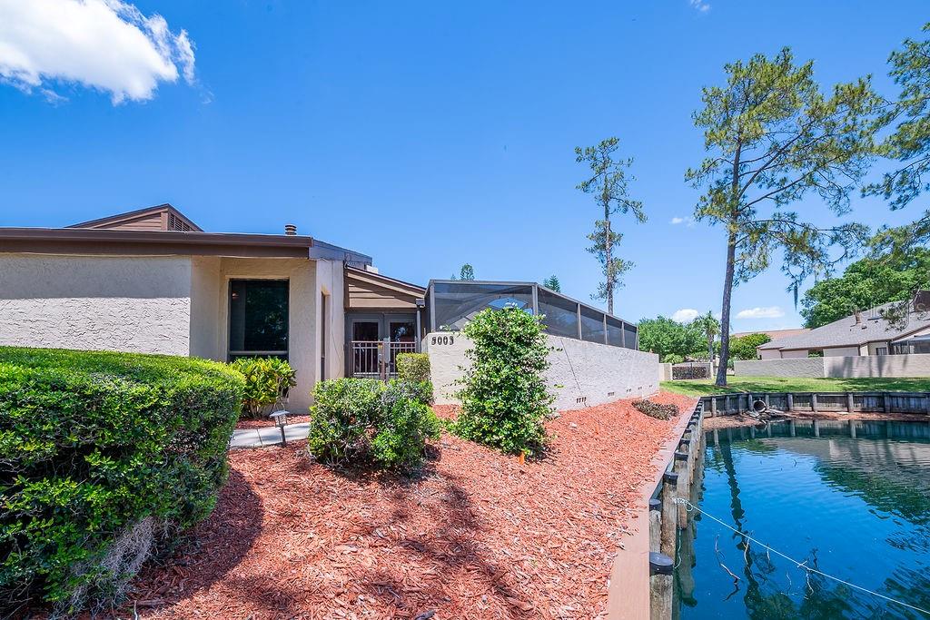 A tan house with a screened-in patio sits next to a small pond — 5003 UMBER WAY S, TAMPA, FL