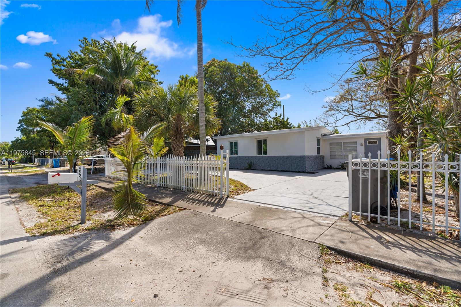A white single-story house with a gray stone base sits behind a white picket fence — 4520 SW 38th St, West Park FL 33023, WEST PARK, FL