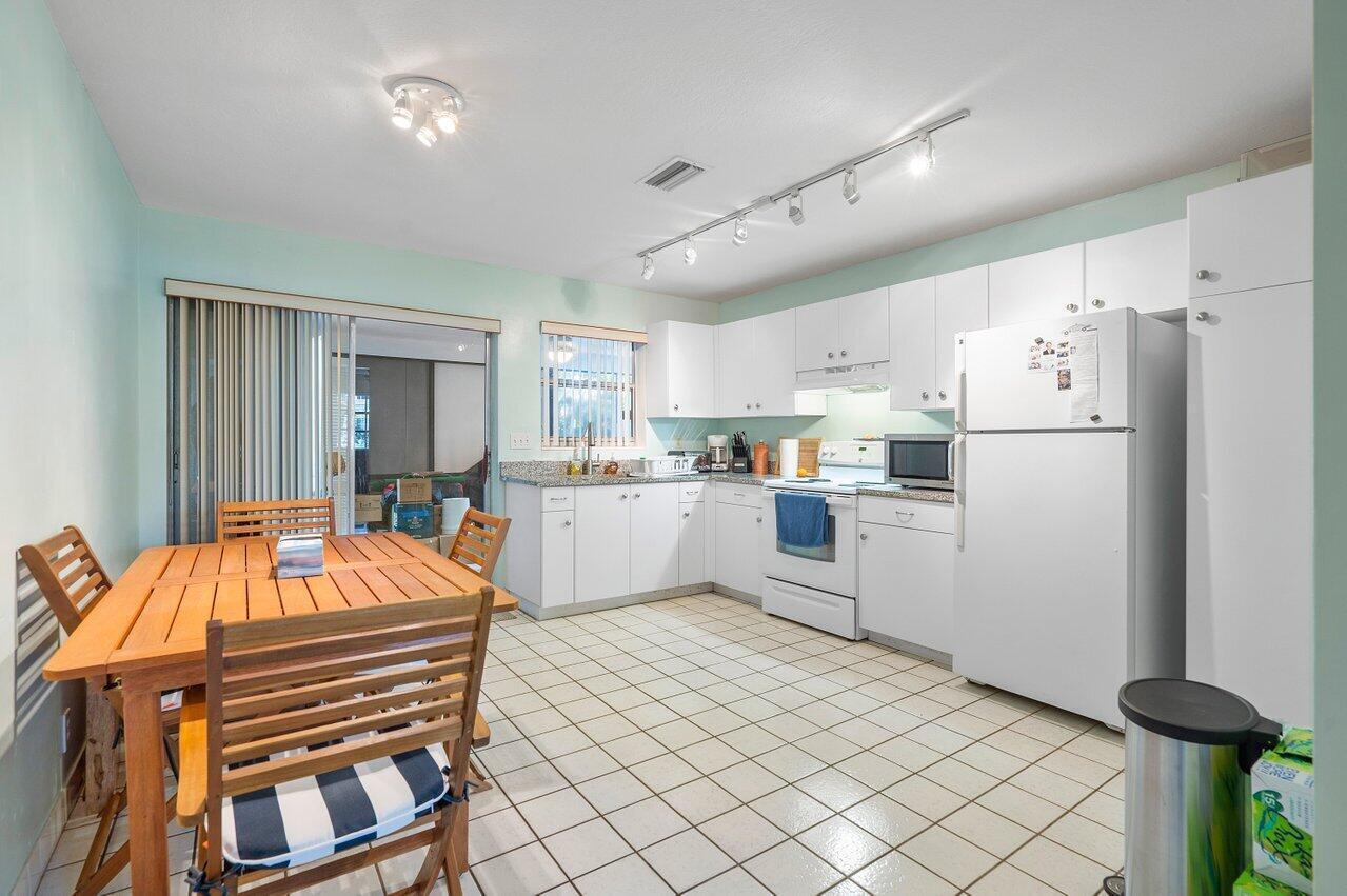 A kitchen with white cabinets, granite countertops, and a dining table in the foreground — 13 Sailfish Lane, Ocean Ridge FL 33435, OCEAN RIDGE, FL