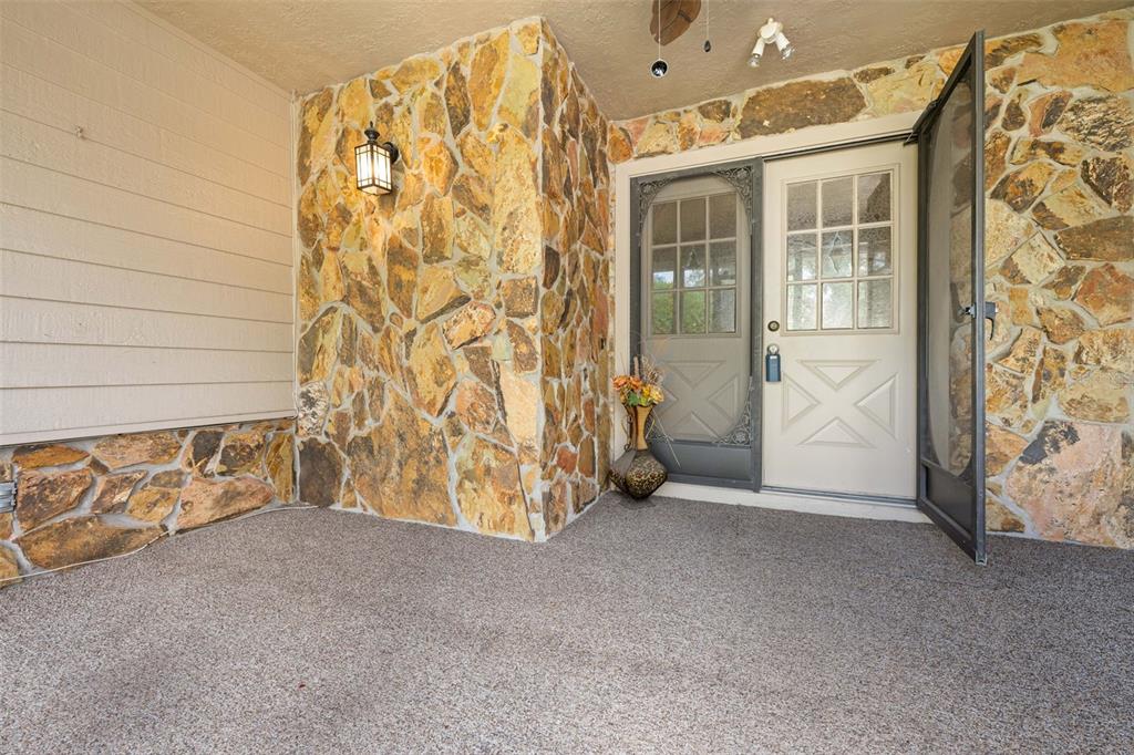 A covered porch features stone walls, a light-colored door with a screen, and textured flooring — 2629 IMPERIAL PINE DRIVE, SPRING HILL, FL