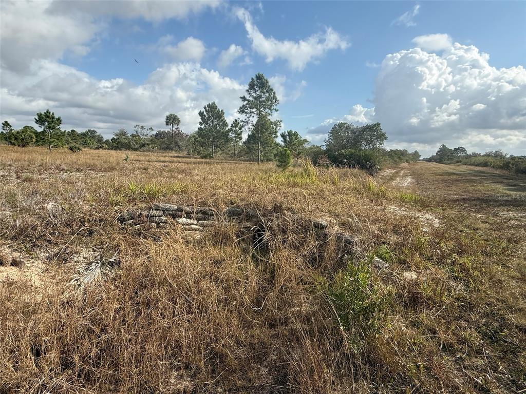 A low stone wall sits in a grassy, undeveloped field under a cloudy sky — 16375 NW 314TH STREET, OKEECHOBEE, FL