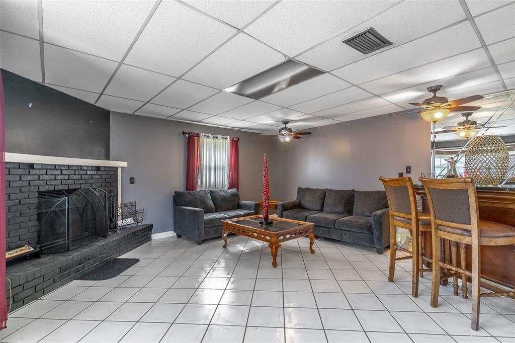 A living room features a black brick fireplace, gray sofas, tile flooring, and a drop ceiling — 3226 KELVINGTON DRIVE, ORLANDO, FL