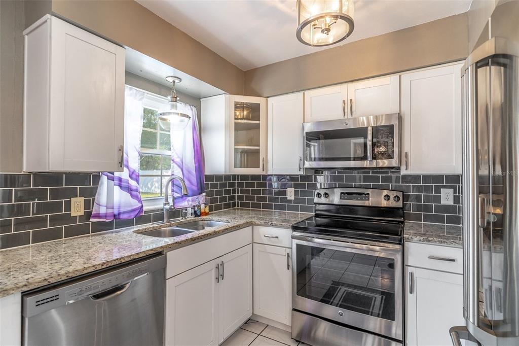 A kitchen with white cabinets, granite countertops, stainless steel appliances, and a gray subway tile backsplash — 3226 KELVINGTON DRIVE, ORLANDO, FL