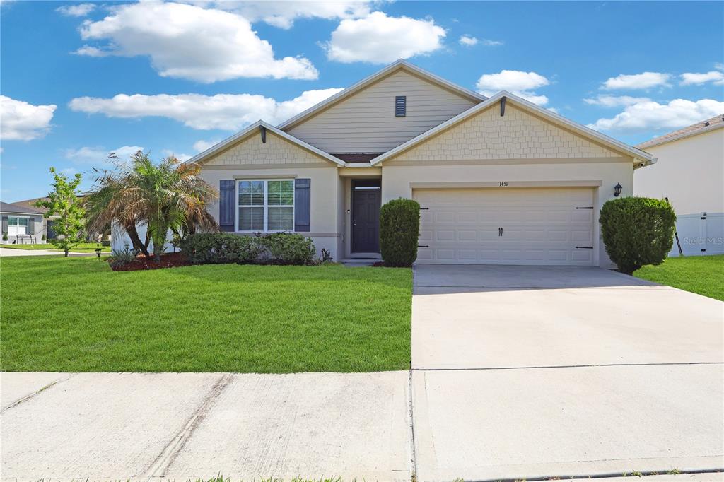 A single-story suburban house features a two-car garage, a front lawn, and a palm tree — 1451 TAOS AVENUE, KISSIMMEE, FL