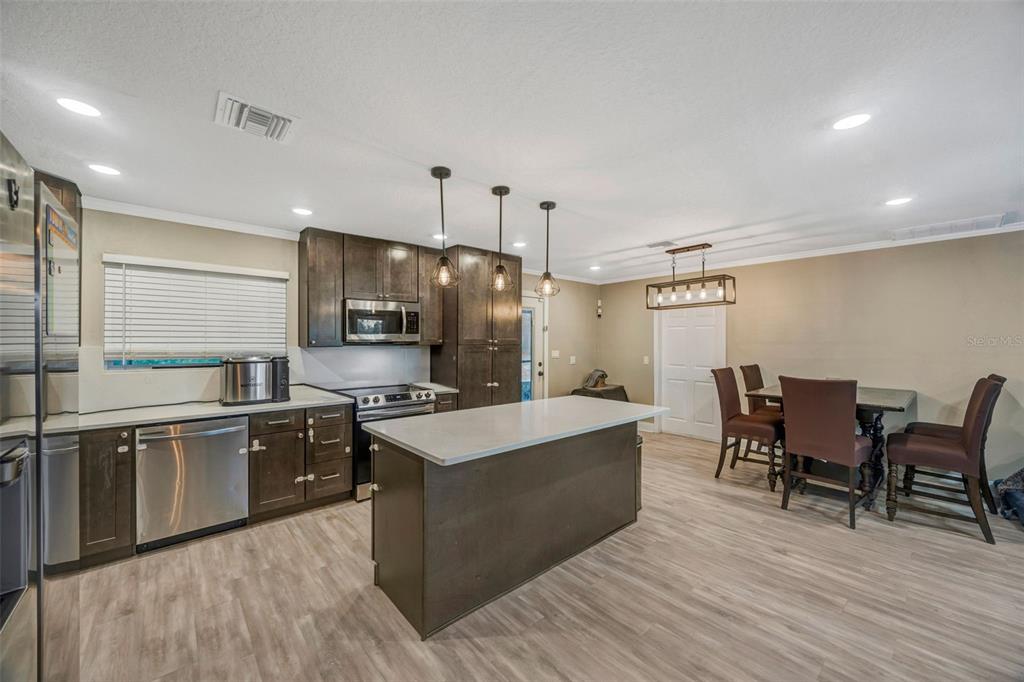 A kitchen features dark wood cabinets, a central island, stainless steel appliances, and dining area — 7149 SPRUCE DRIVE, WEEKI WACHEE, FL