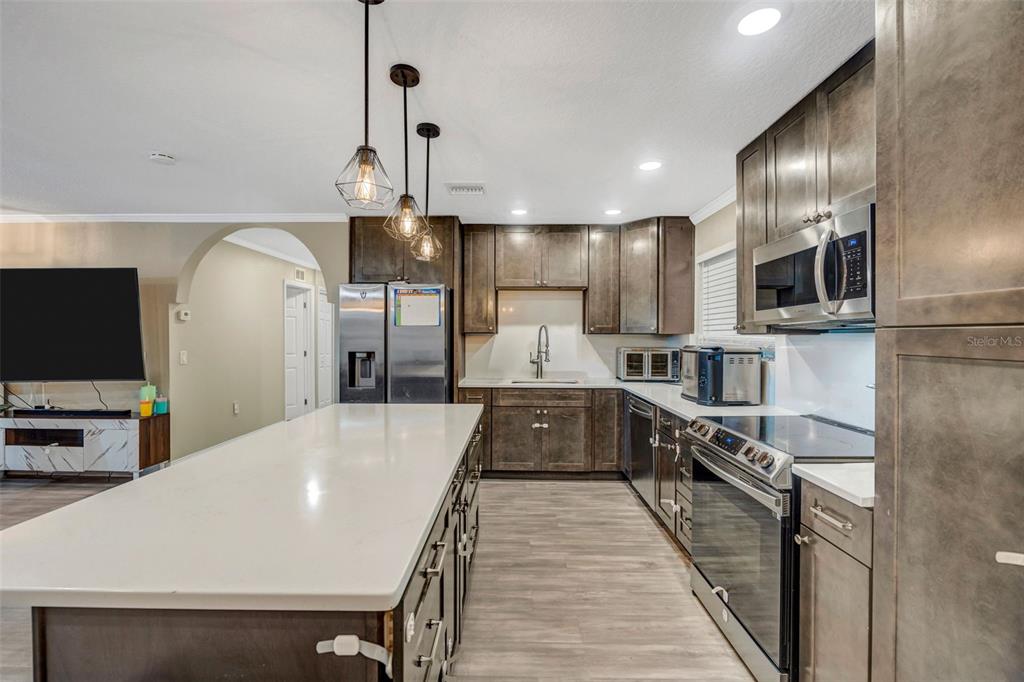 A modern kitchen features dark wood cabinets, a large white island, and stainless steel appliances — 7149 SPRUCE DRIVE, WEEKI WACHEE, FL