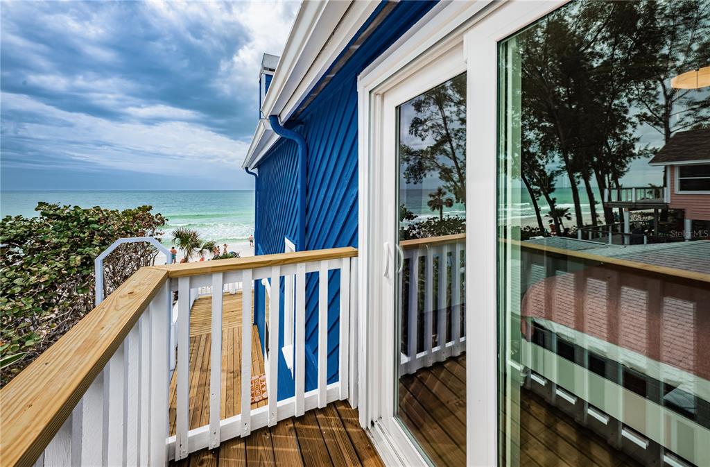 A wooden balcony with a white railing overlooks the ocean next to a blue house — 8432 W GULF BOULEVARD UNIT Sailfish, TREASURE ISLAND, FL