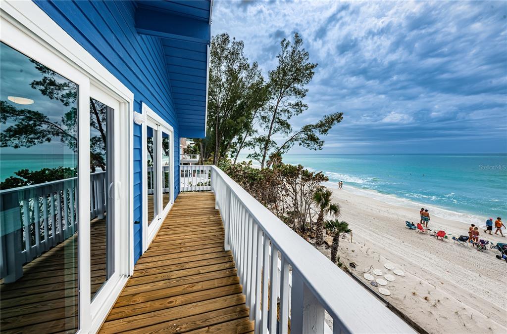 A blue house features a wooden balcony overlooking a sandy beach and the ocean — 8432 W GULF BOULEVARD UNIT Sailfish, TREASURE ISLAND, FL
