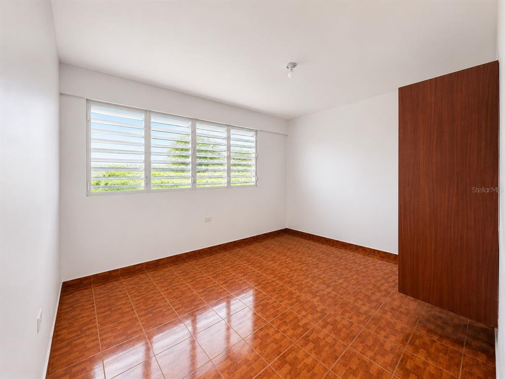 An empty bedroom features white walls, brown tiled flooring, a louvered window, and a wooden closet — CARR. 908 KM 9.4 BO. TEJAS APT. UNIT 7, HUMACAO, PR
