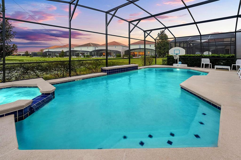 A screened-in swimming pool and hot tub overlook a grassy field at sunset — 8013 OAK SHADOW COURT, DAVENPORT, FL