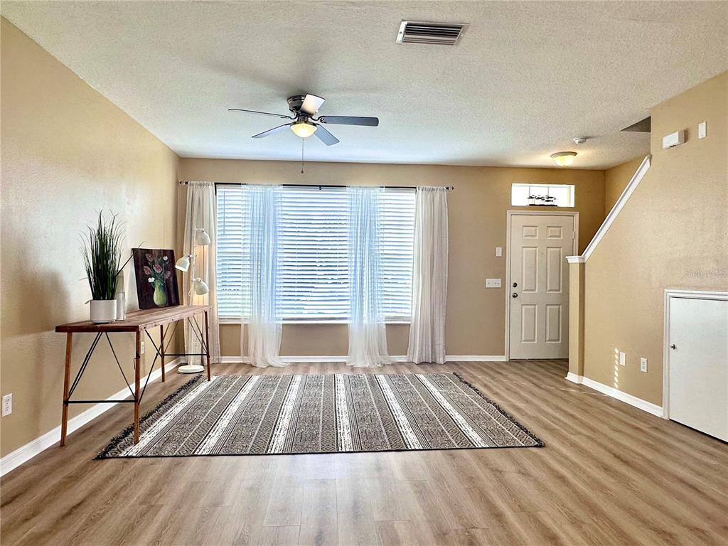 A living room features wood-look flooring, a ceiling fan, a large window, and a rug — 12276 COUNTRY WHITE CIRCLE, TAMPA, FL