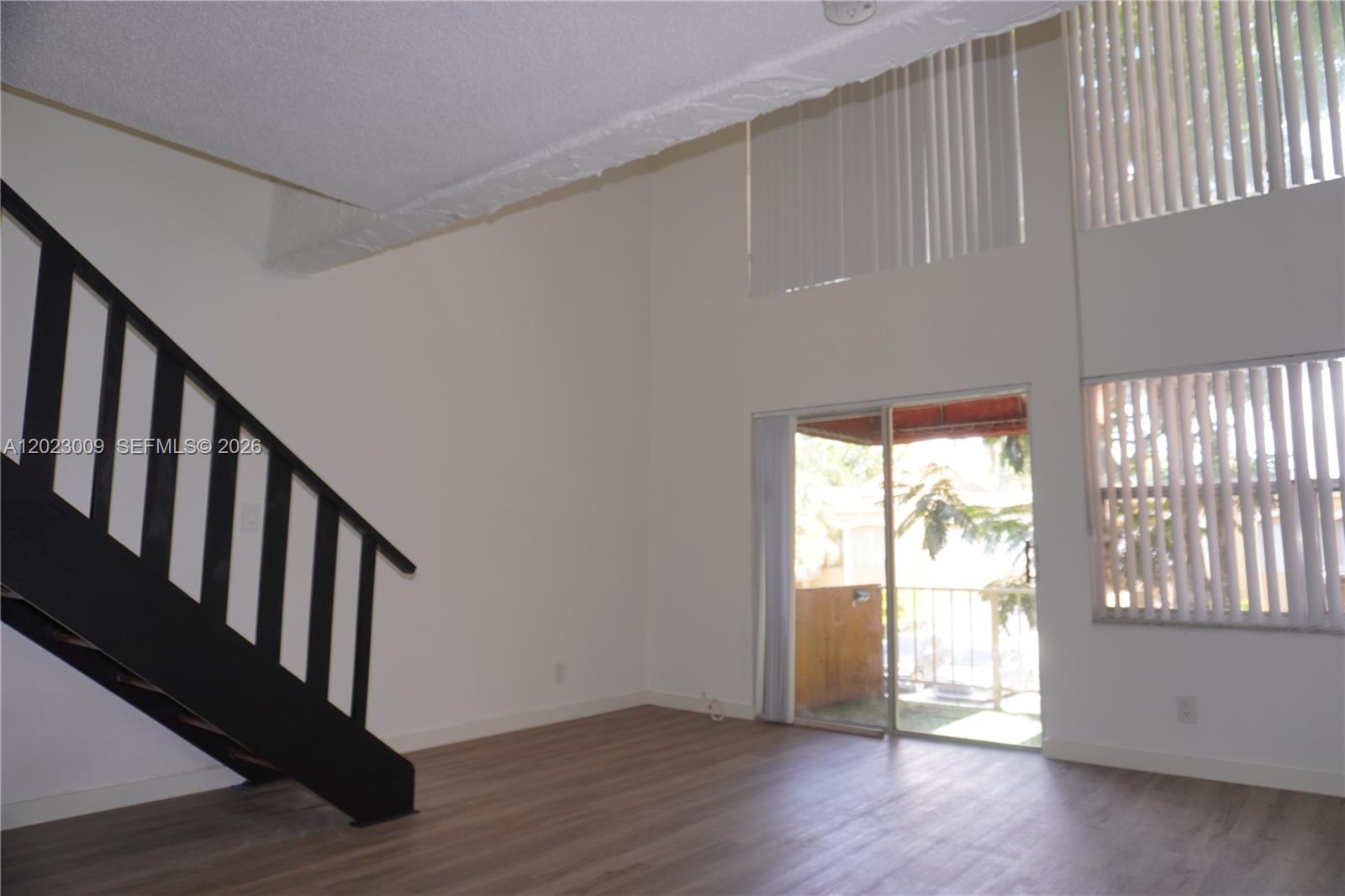A living room features high ceilings, wood-look flooring, a black staircase, and sliding glass doors — 17901 NW 68th Ave # S204, Hialeah FL 33015, HIALEAH, FL