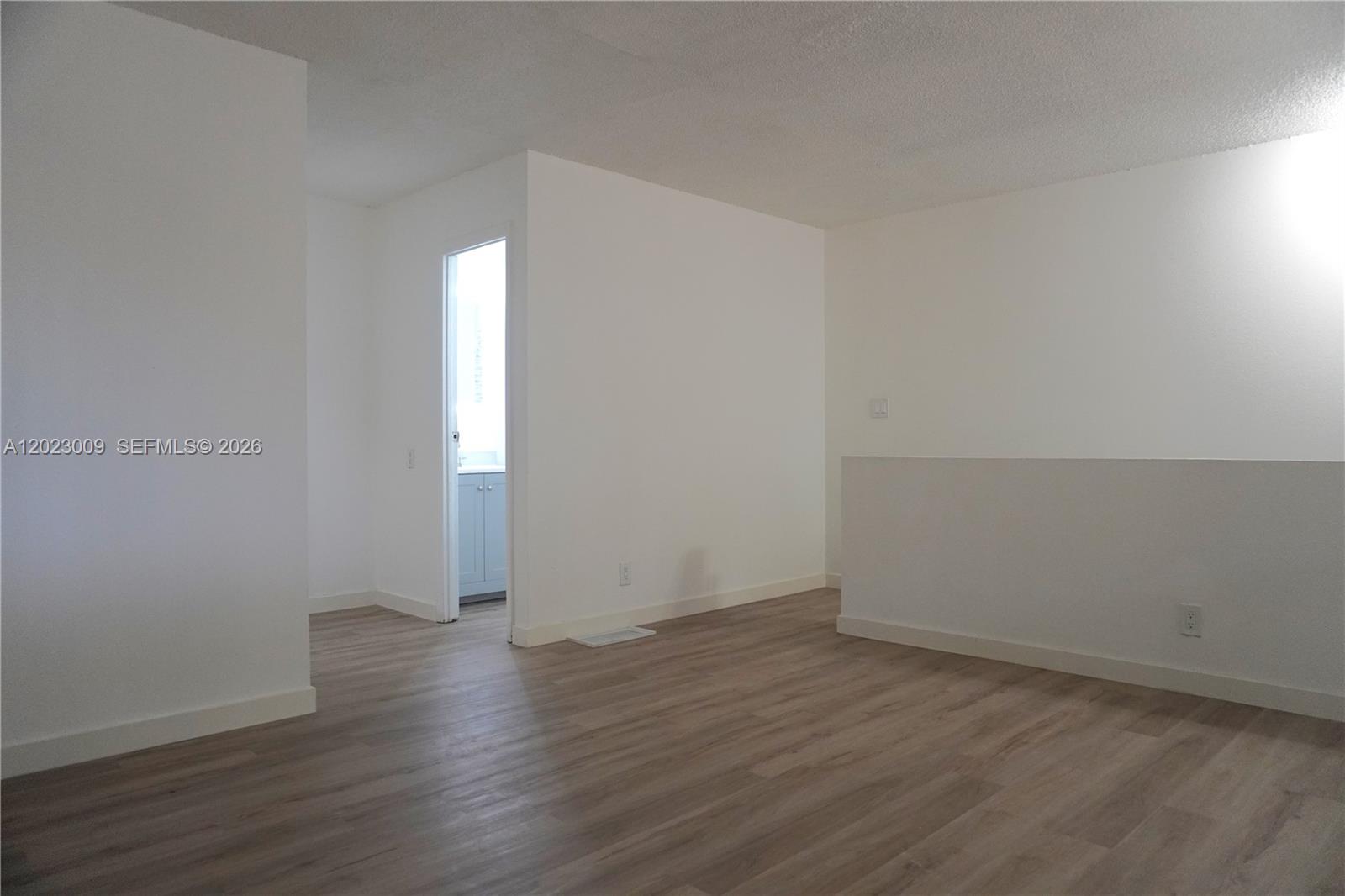 An empty room features light wood-look flooring, white walls, and a doorway leading to a bathroom — 17901 NW 68th Ave # S204, Hialeah FL 33015, HIALEAH, FL