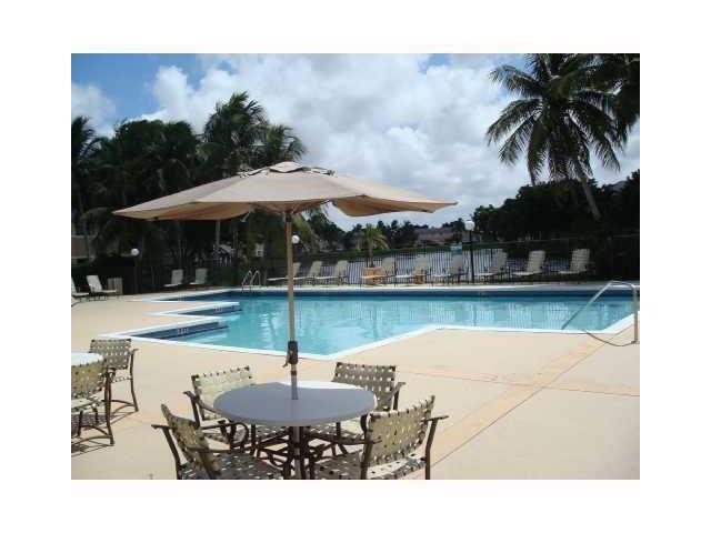 A swimming pool area features a patio with a table, umbrella, and lounge chairs — 417 E Palm Cir Circle E # 417, Pembroke Pines FL 33025, PEMBROKE PINES, FL