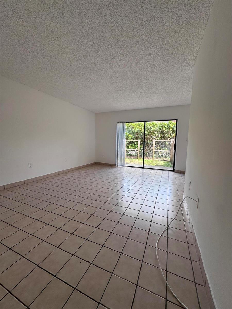 An empty room with light-colored tile flooring and a sliding glass door leading outside — 417 E Palm Cir Circle E # 417, Pembroke Pines FL 33025, PEMBROKE PINES, FL