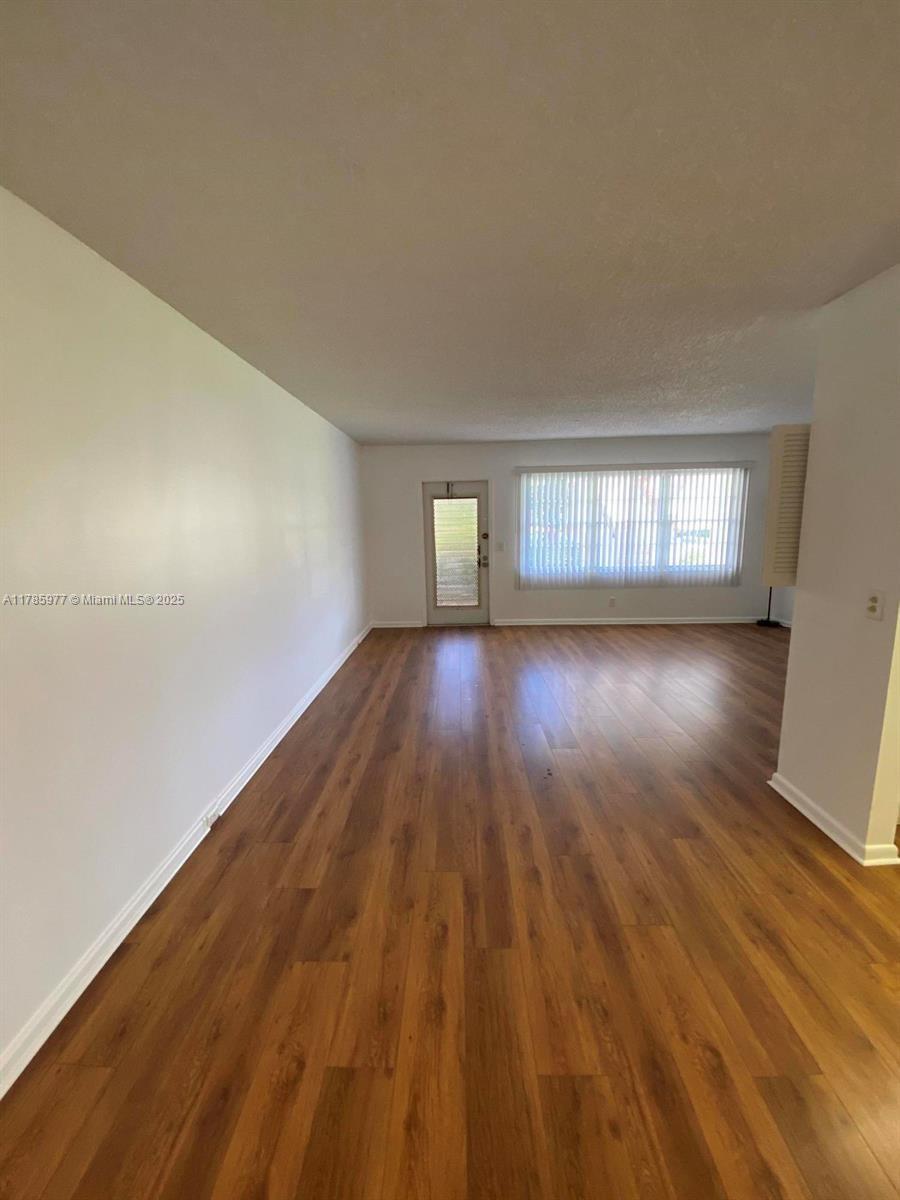 An empty living room features wood-look flooring, white walls, a glass door, and vertical blinds — 381 Fanshaw J # 381, Boca Raton FL 33434, BOCA RATON, FL