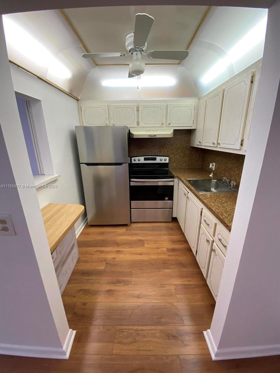 A galley kitchen features white cabinets, stainless steel appliances, and wood-look flooring — 381 Fanshaw J # 381, Boca Raton FL 33434, BOCA RATON, FL