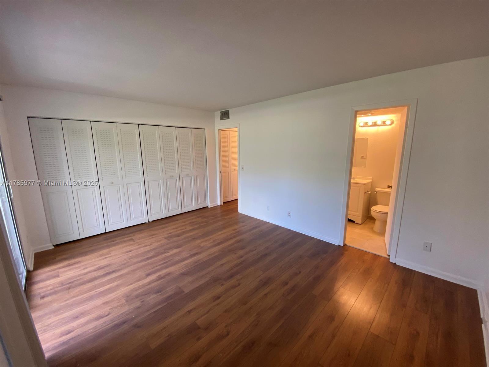 A bedroom features wood-look flooring, a large white closet, and an attached bathroom — 381 Fanshaw J # 381, Boca Raton FL 33434, BOCA RATON, FL