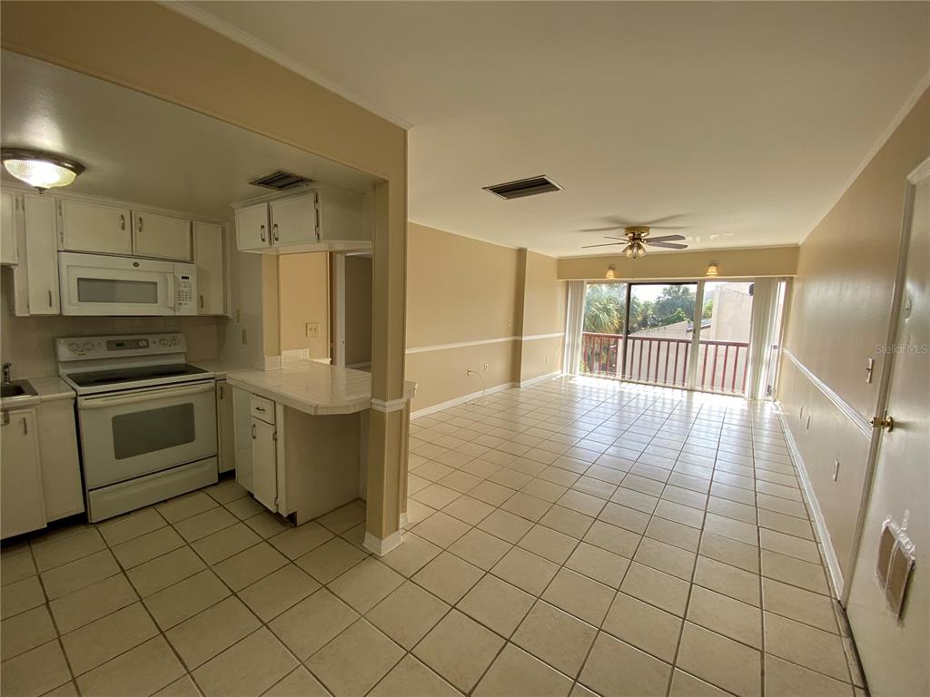 A kitchen with white cabinets and appliances opens into a tiled living area with a balcony — 8602 HURON COURT UNIT 50, TAMPA, FL