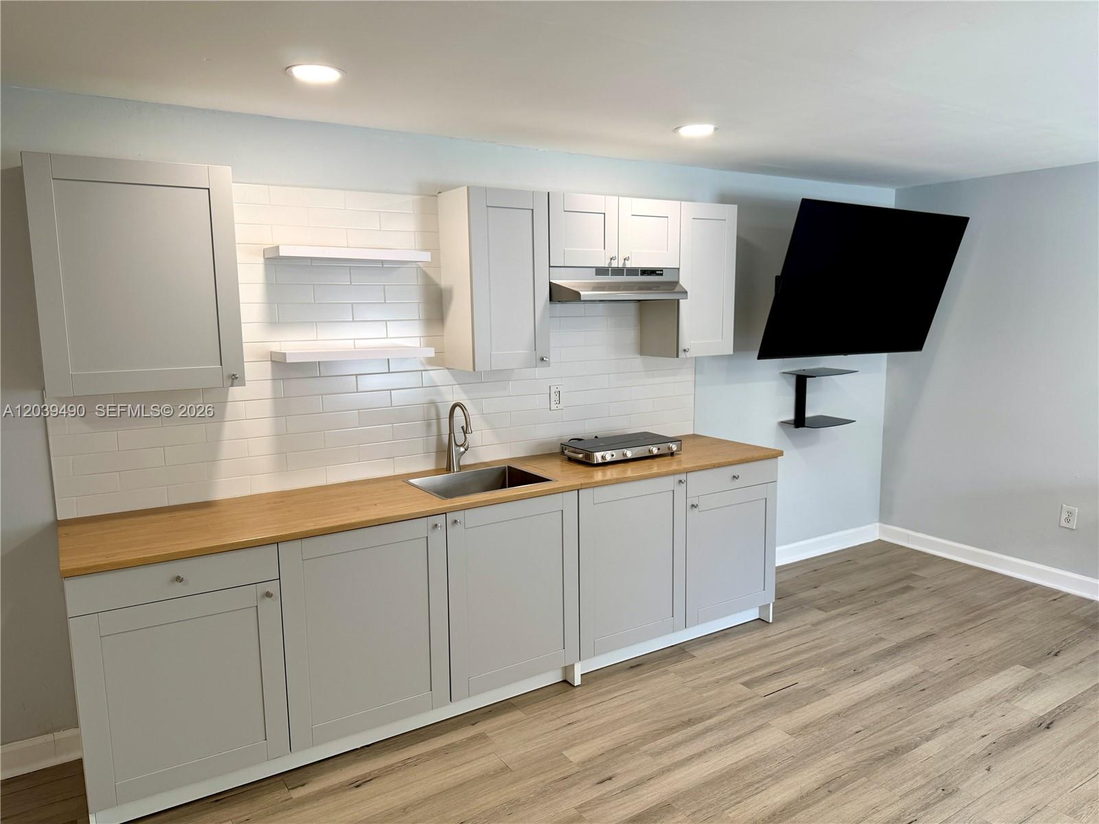 A kitchen features light gray cabinets, a wood countertop, white subway tile, and a wall-mounted television — 227 SW 26th Rd Rear, Miami FL 33129, MIAMI, FL