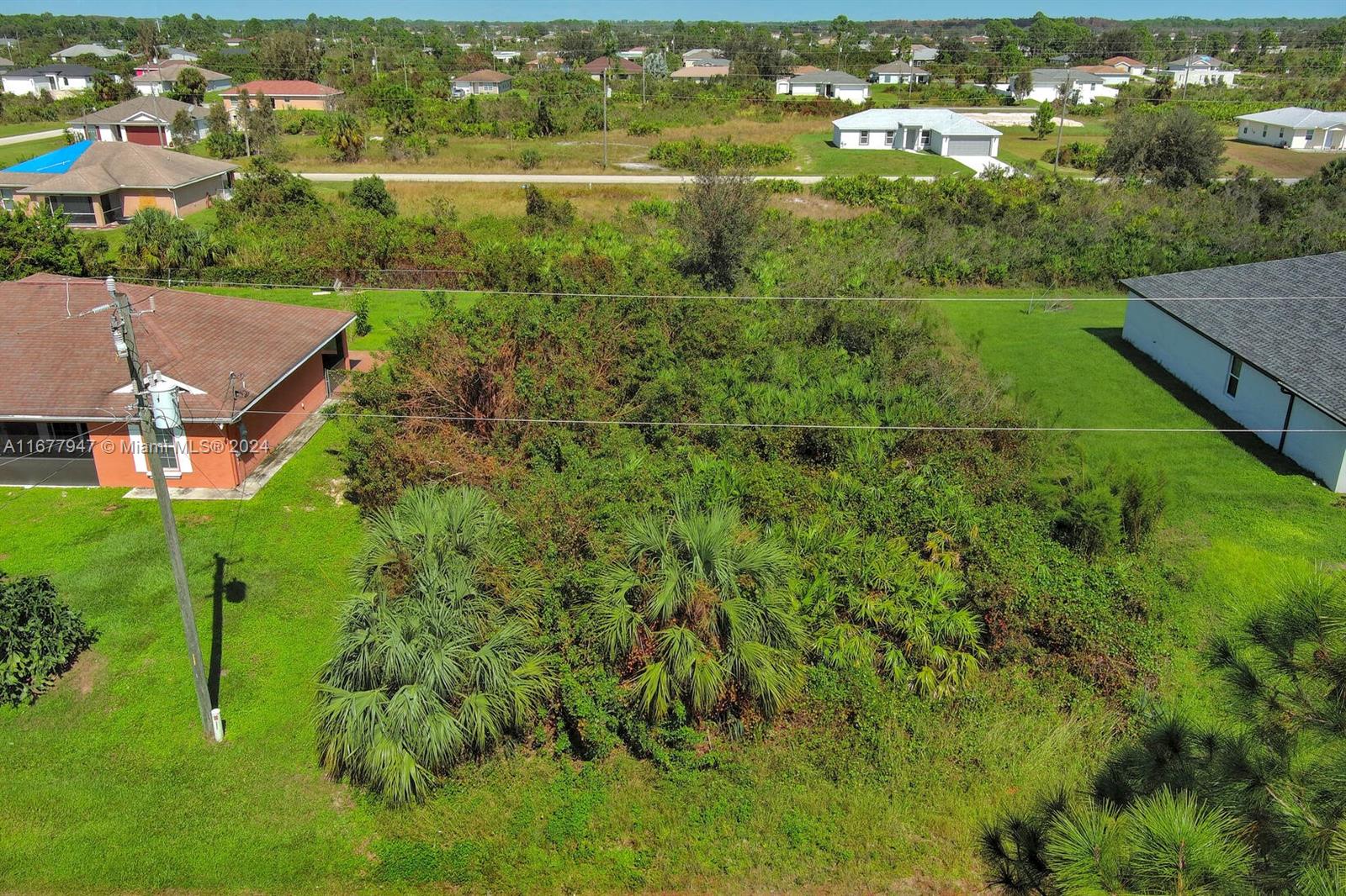 An aerial view shows a vacant, overgrown residential lot situated between two existing houses — 2912 61st St W, Lehigh Acres FL 33971, LEHIGH ACRES, FL