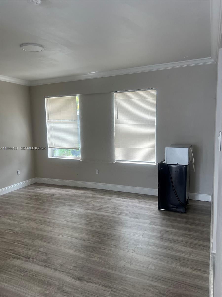 An empty room features light gray walls, wood-look flooring, two windows with blinds, and a mini-fridge — FORT LAUDERDALE, FL
