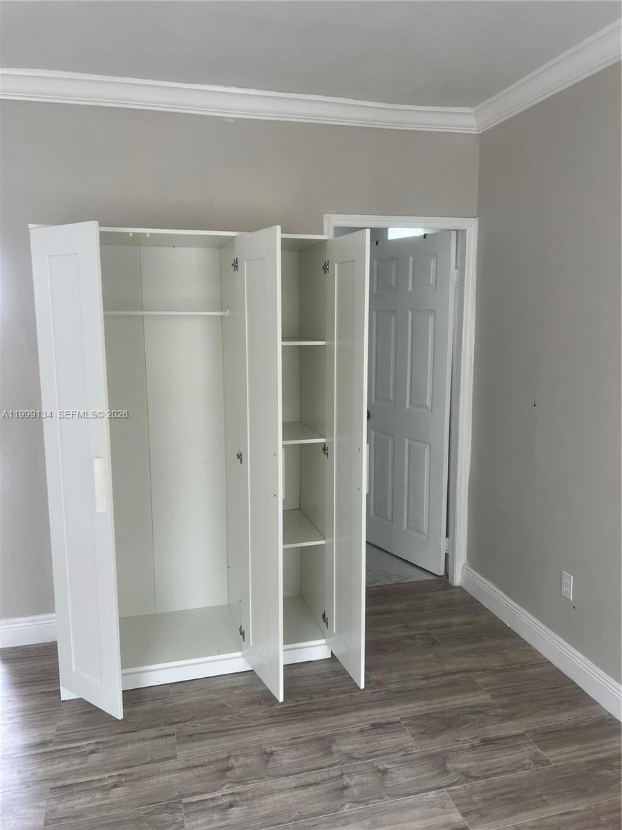 A white wardrobe stands in a room with gray walls and wood-look flooring — FORT LAUDERDALE, FL