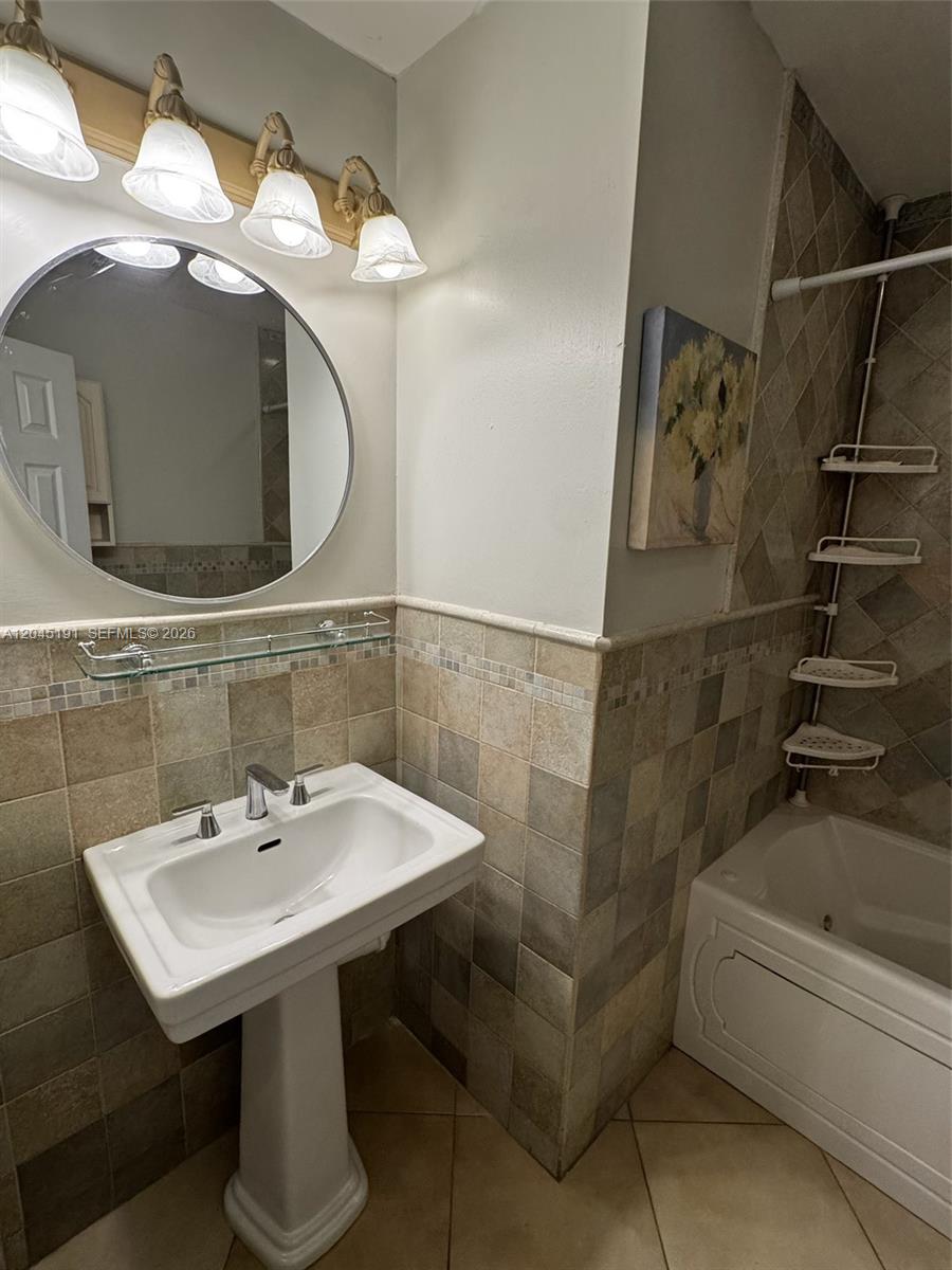A bathroom features a pedestal sink, a round mirror, and tiled walls near a tub — 158 SW 96th Ct # B, Miami FL 33174, MIAMI, FL