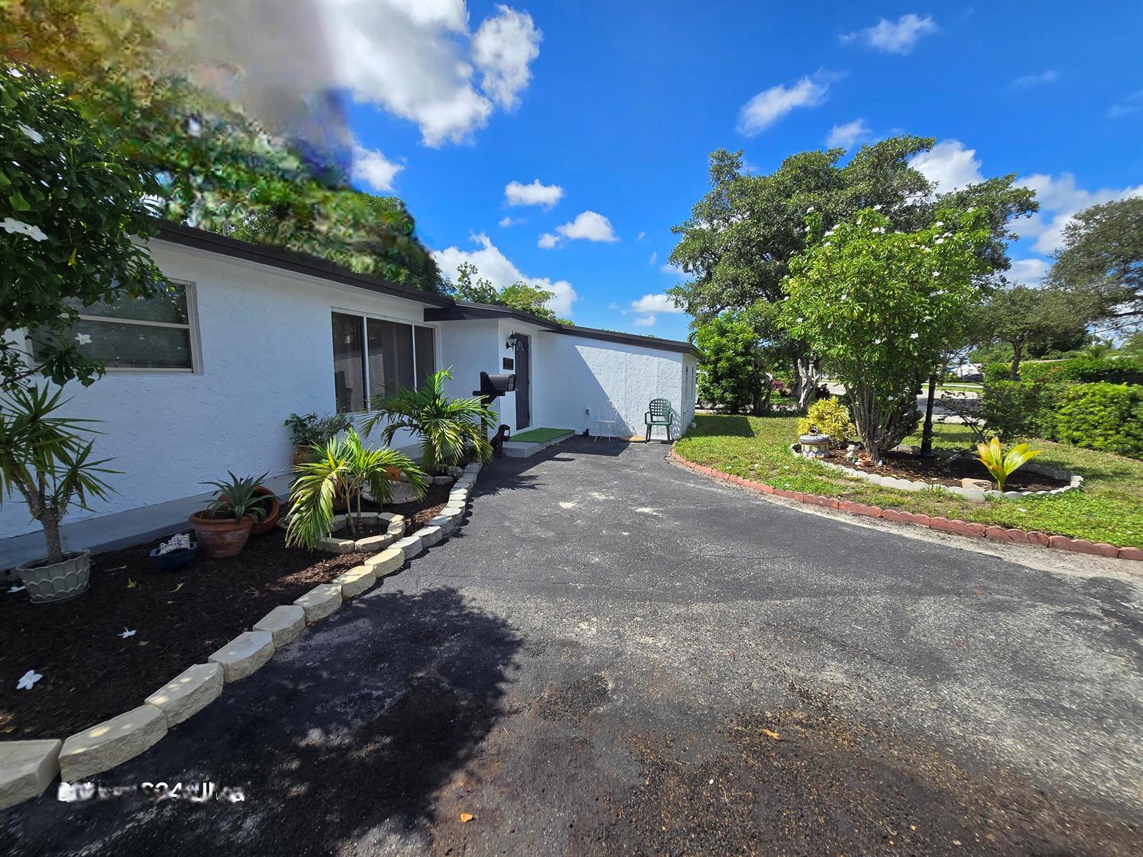 A white house with a dark roof features a paved driveway and landscaped garden beds — 6138 Southgate Boulevard, Margate FL 33068, MARGATE, FL