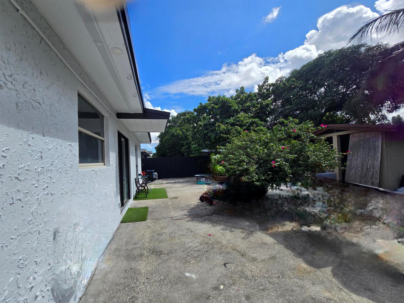 A concrete patio area sits beside a white stucco house under a blue sky — 6138 Southgate Boulevard, Margate FL 33068, MARGATE, FL