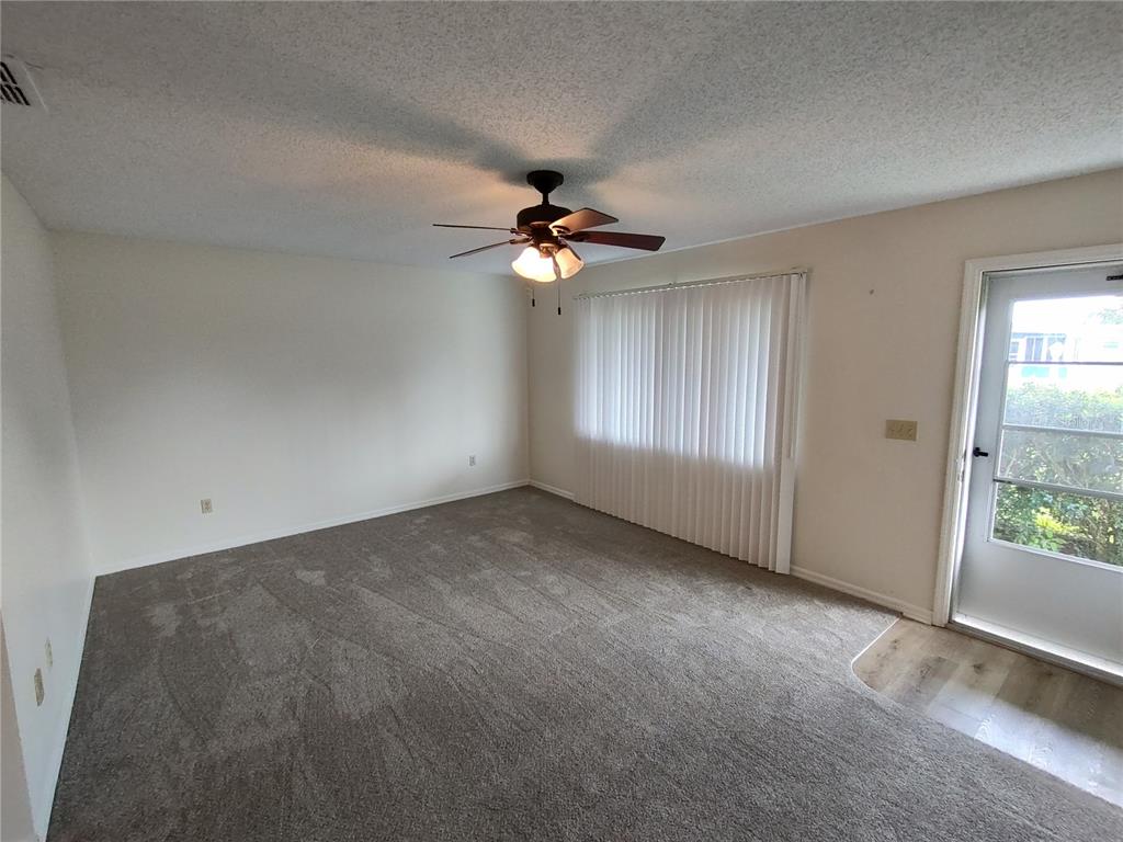 A living room with gray carpet, a ceiling fan, vertical blinds, and a glass door — 6429 SW 107TH STREET, OCALA, FL