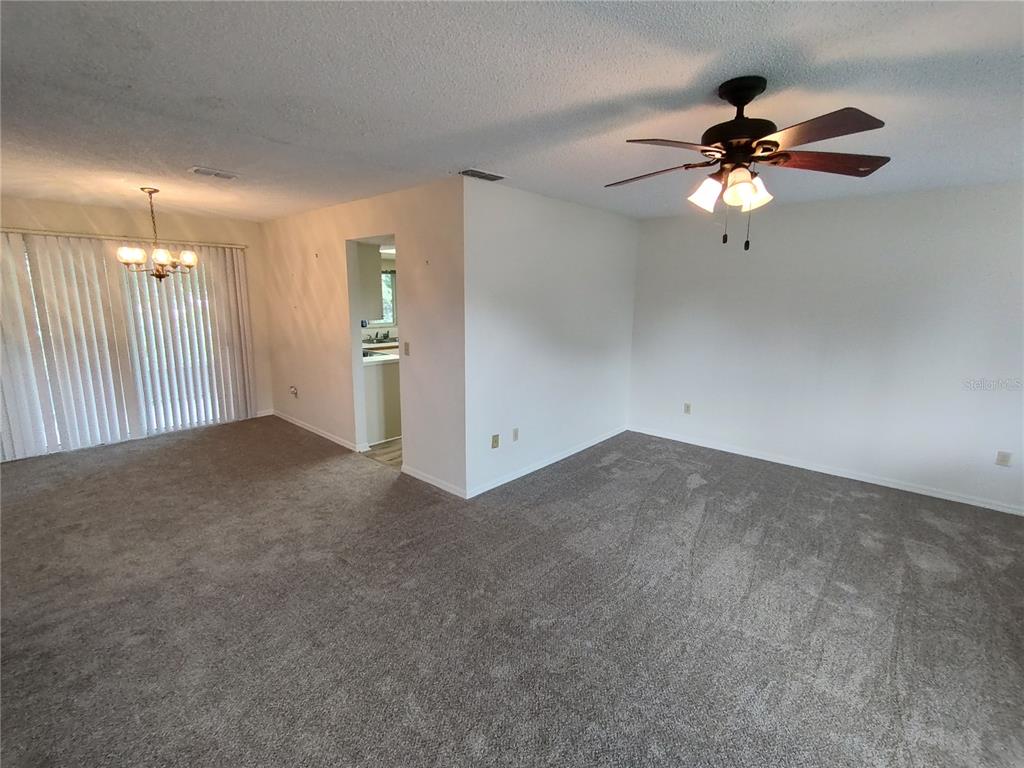 A carpeted living room features a ceiling fan, a dining area, and a sliding glass door — 6429 SW 107TH STREET, OCALA, FL