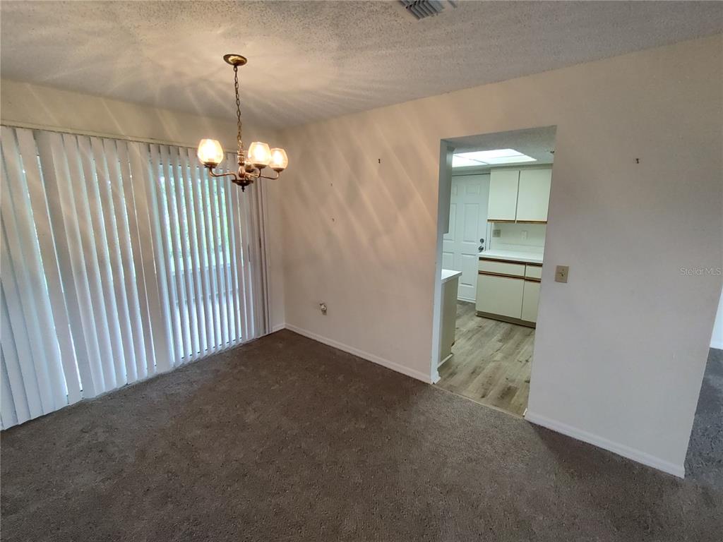 A dining area with carpeted flooring, a chandelier, and a doorway leading to a kitchen — 6429 SW 107TH STREET, OCALA, FL
