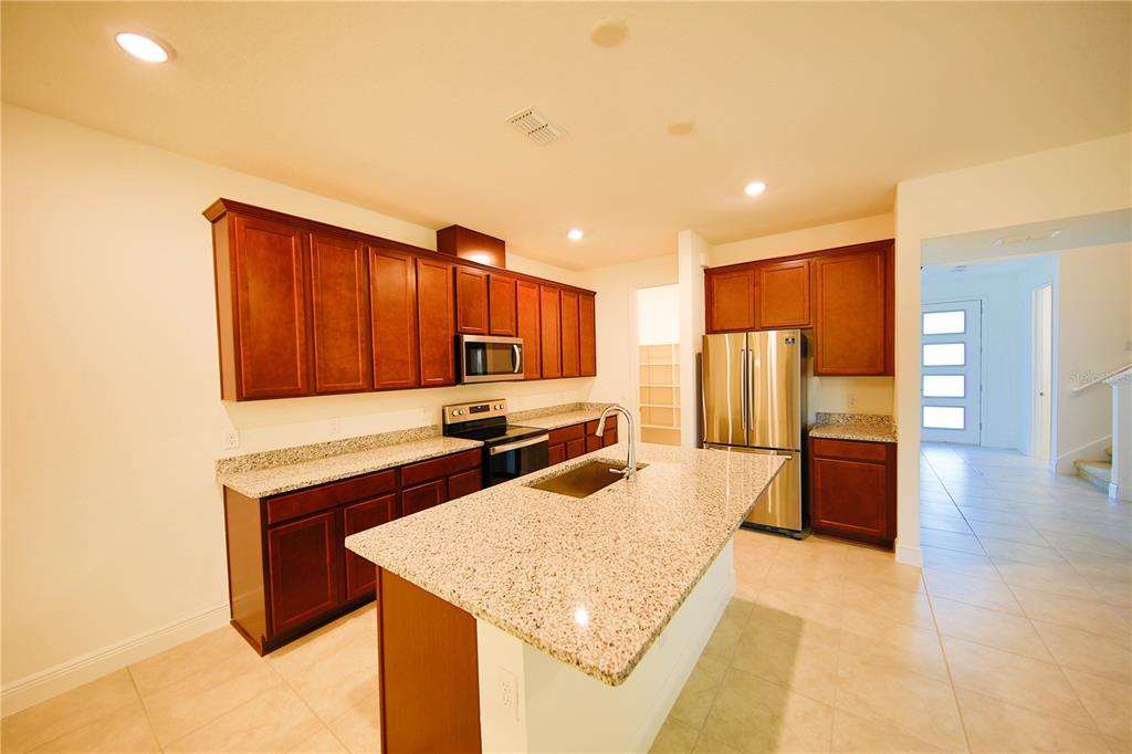 A kitchen features dark wood cabinets, granite countertops, stainless steel appliances, and a central island — 7389 ALPINE BUTTERFLY LANE, ORLANDO, FL