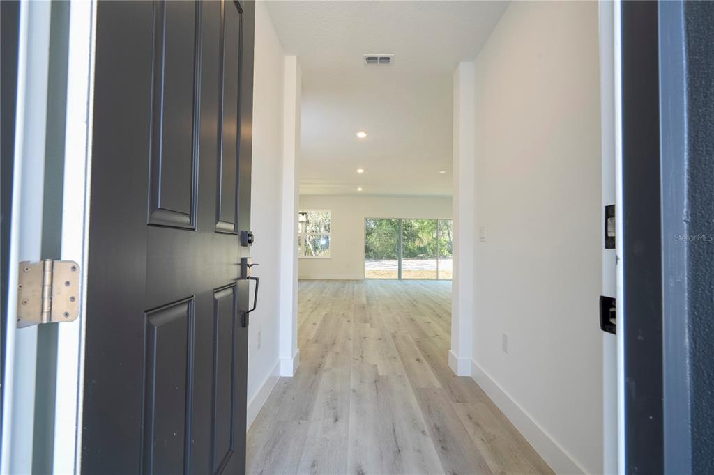 A view through an open front door into a bright, empty home with wood-look flooring — 42065 TAMARAC STREET, EUSTIS, FL