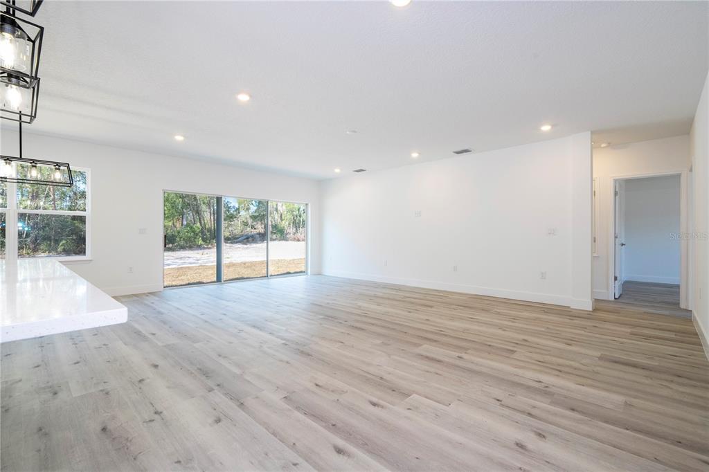 A bright, open-concept living area features light wood-look flooring, white walls, and sliding glass doors — 42065 TAMARAC STREET, EUSTIS, FL