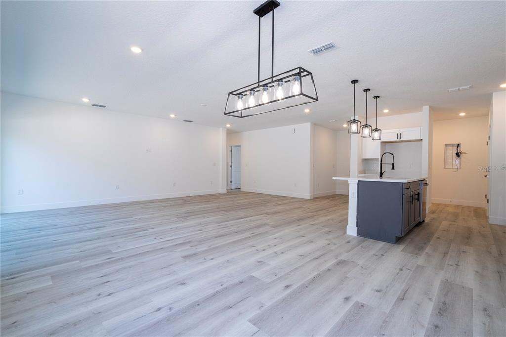 An open-concept living area features light wood-look flooring, a kitchen island, and modern pendant lighting — 42065 TAMARAC STREET, EUSTIS, FL